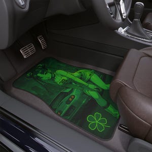 May include: Green car floor mat featuring a stylized anime character in green attire, lying near a car graphic. The mat has a dark green background with a four-leaf clover design. The mat is placed in a car interior.