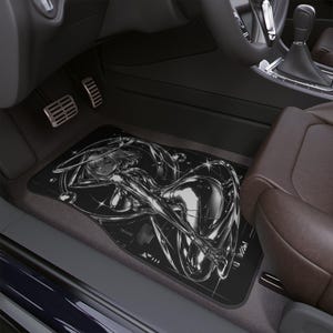 May include: Black car floor mat featuring a chrome-like illustration of a female figure in a futuristic design. The mat is rectangular and fits in the driver's side footwell of a car. The car interior is black and brown.