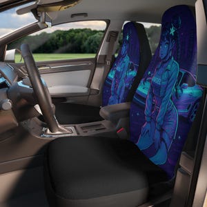 May include: Car seat covers featuring a vibrant anime-style illustration of a woman and a sports car. The design uses a palette of blues and purples with the word "ANGEL" visible on the jacket. The covers are installed in a car interior.