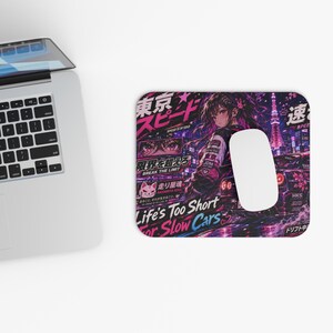 Puede incluir: Alfombrilla de ratón rectangular con un diseño colorido de estilo anime. El diseño presenta una mujer, texto japonés y la frase "Life's Too Short For Slow Cars". Se ve un ordenador portátil.