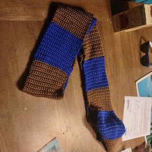 May include: A brown and blue striped crocheted scarf. The scarf is made with a simple stitch and has a long, flowing shape.
