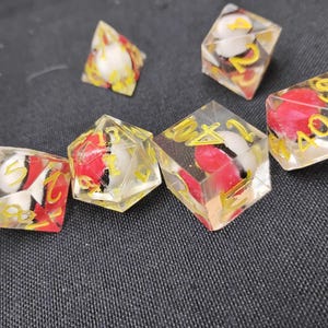 May include: Six clear dice with red and white marbled interiors and yellow numbers. The dice are on a black surface.