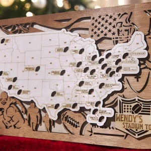 May include: A wooden map of the United States with a football stadium icon for each state. The map is surrounded by a wooden frame with a cutout of a football player. The bottom of the map features a wooden sign that reads "WENDY'S STADIUM TOUR".