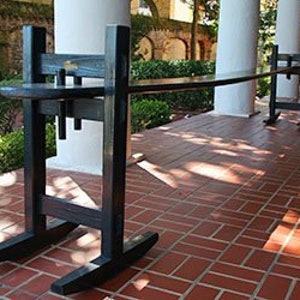 May include: A long, black wooden table with a unique design. The table is supported by two sets of rocking legs, giving it a whimsical look. The table is made of dark wood and has a smooth, polished finish.