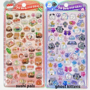 Puede incluir: Dos hojas de pegatinas con pegatinas transparentes y brillantes. Una hoja presenta dise&ntilde;os de sushi y gatos con el texto "sushi pals". La otra hoja tiene dise&ntilde;os de fantasmas y gatitos con el texto "ghost kittens". Ambas tienen el texto "うるちゅる POP SEAL."
