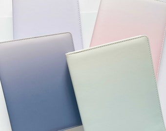 May include: Four different colored notebooks with a gradient design. The notebooks are all closed and have a stitched edge. The colors are light purple, light pink, light blue, and light green.
