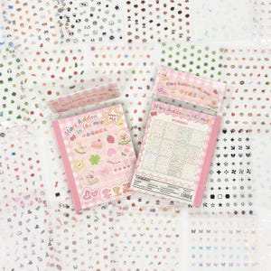 May include: A collection of sticker sheets with various designs, including stars, hearts, and small illustrations of animals and food. Two pink-covered sticker books are visible, with text that reads "Stars Aidden in the mist".