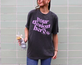 May include: A black t-shirt with the text "your design here" in pink lettering. The shirt is being worn by a person standing in front of a green tiled wall.