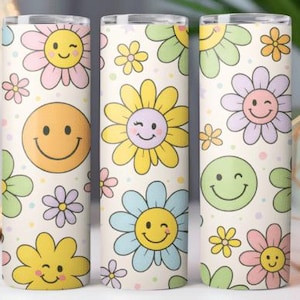 May include: Three cylindrical tumblers with a repeating pattern of smiling flowers and smiley faces in pastel colors on a cream background. The flowers are in shades of yellow, pink, blue, and green. The tumblers are likely for beverages.