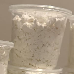 May include: Clear plastic containers filled with white, crumbly food product. The containers have clear lids and are stacked on top of each other. The food product appears to be cottage cheese or a similar dairy product.