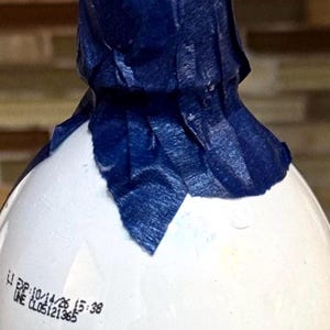 May include: A white bottle with a blue paper covering the top. The bottle has a label with the text "LI DP: 10/14/26 15:38 UNE CLOS:121365".
