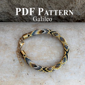 May include: A beaded bracelet with a gold, black and silver pattern. The bracelet has a gold clasp and is labelled "PDF PATTERN Galileo".