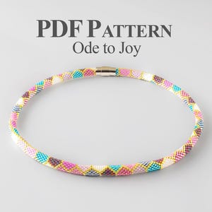 May include: A beaded necklace with a geometric pattern in shades of pink, teal, white, gold, and gray. The necklace has a magnetic clasp and the text "PDF PATTERN Ode to Joy" is above the necklace.