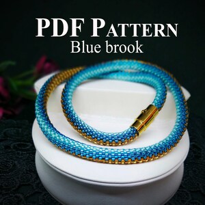 Puede incluir: Patrón PDF para un collar y una pulsera de cuentas en tonos azules y dorados. El collar tiene un cierre dorado. El texto "PDF PATTERN Blue brook" está en la parte superior de la imagen.