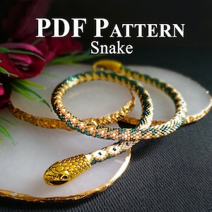 May include: A PDF pattern for a beaded snake, featuring a green, white and gold colour scheme. The snake is coiled on a white surface with a gold rim.