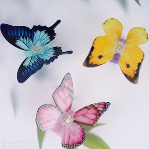 May include: Three butterfly hair clips. One is blue and black, one is yellow and black, and one is pink and black.