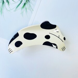 May include: A white and black ceramic hair clip shaped like a sleeping dalmatian dog.