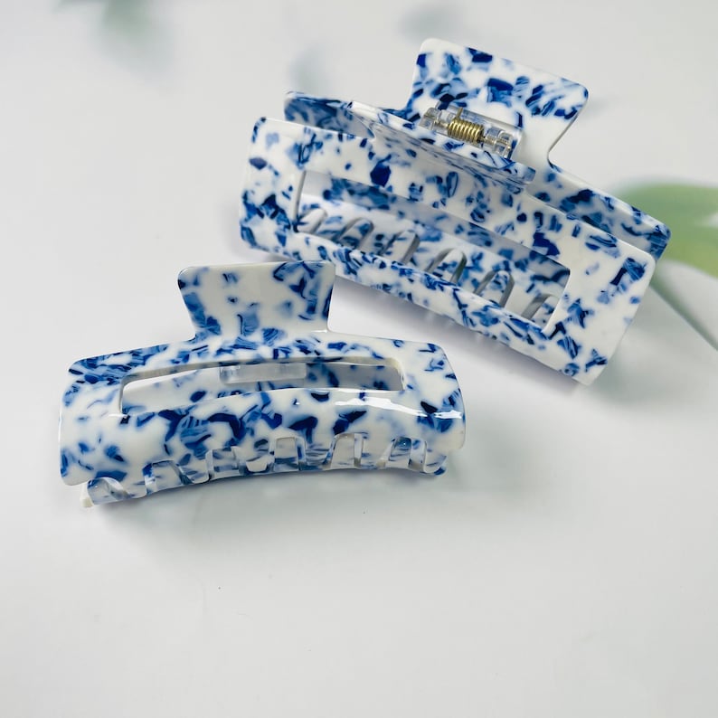 K&ouml;nnte beinhalten: Zwei blaue und wei&szlig;e gemusterte Haarklammern. Die Klammern sind aus Kunststoff und haben ein Klauen-Design.