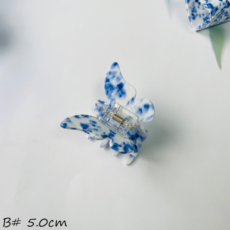 K&ouml;nnte beinhalten: Blau-wei&szlig;er Schmetterlings-Haarklammer mit Federspanner. Die Klammer ist 5,0 cm gro&szlig;.