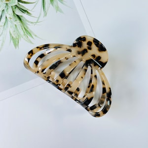 May include: A large, brown and black tortoise shell hair claw clip. The clip is made of plastic and has a curved shape.