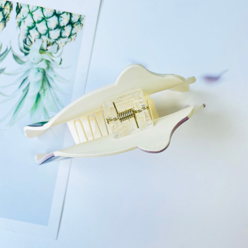 May include: A white plastic hair claw with a clear plastic spring mechanism. The claw has a smooth, rounded shape and a textured grip.