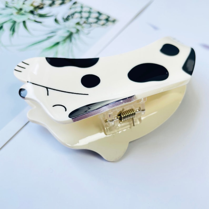 May include: A white and black spotted plastic hair clip with a spring-loaded clasp. The clip is shaped like a cartoon dog.