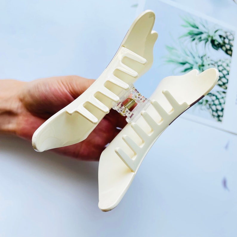 May include: A white plastic hair claw with a clear plastic spring mechanism. The claw is designed to hold hair in place.