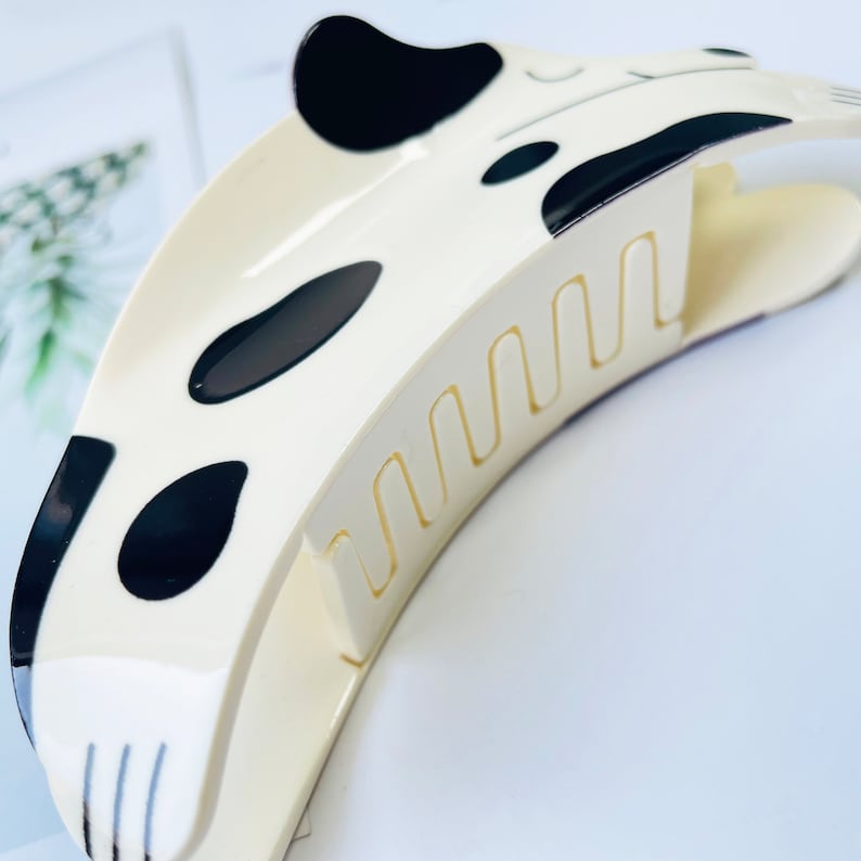 May include: White plastic hair claw with a black and white dalmatian dog design. The claw has a series of teeth on the underside to hold hair in place.