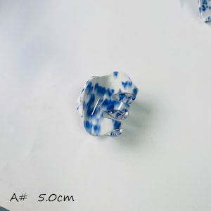 K&ouml;nnte beinhalten: Eine wei&szlig;e und blaue Haarklammer mit einem blauen und wei&szlig;en Wirbelmuster. Die Klammer ist 5,0 cm lang.