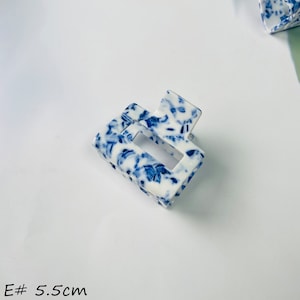 K&ouml;nnte beinhalten: Eine wei&szlig;e und blaue gemusterte Haarklammer mit einer rechteckigen &Ouml;ffnung. Die Klammer ist 5,5 cm lang.