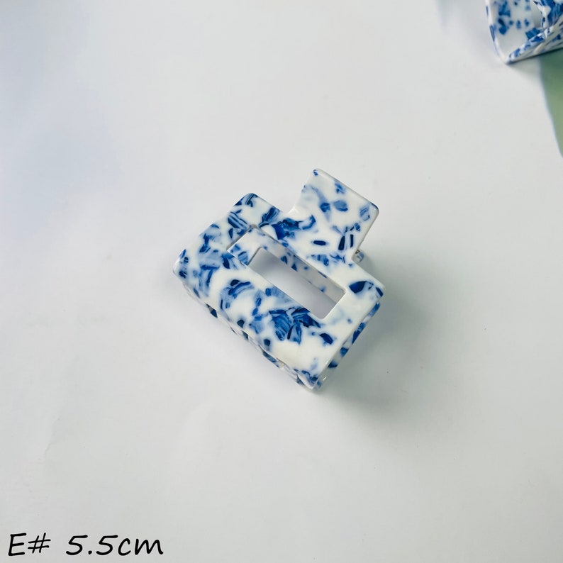 K&ouml;nnte beinhalten: Eine wei&szlig;e und blaue gemusterte Haarklammer mit einer rechteckigen &Ouml;ffnung. Die Klammer ist 5,5 cm lang.