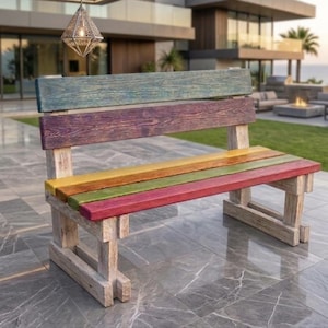 May include: A wooden bench featuring a backrest with a teal top plank and a purple lower plank. The seat consists of three horizontal planks in yellow, green, and red. The frame and legs are constructed from light-colored, weathered wood planks.