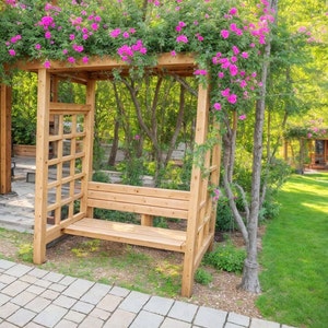 May include: A wooden bench with a slatted back and seat is situated under a pergola covered in pink climbing roses. The pergola is made of natural wood and has a lattice design. The bench is surrounded by green grass and a stone path.