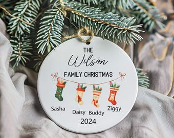 May include: White ceramic Christmas bauble featuring the text "The Wilson Family Christmas" and four stockings with the names Sasha, Daisy, Buddy, and Ziggy. The year 2024 is printed below the stockings.