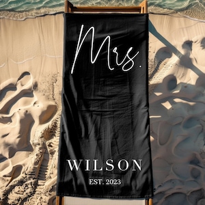 May include: Black beach towel with white text that reads "Mrs. Wilson EST. 2023".