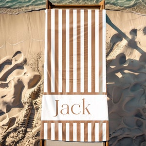 Puede incluir: Una toalla de playa a rayas marrones y blancas con el nombre "Jack" impreso en marr&oacute;n sobre una raya blanca.