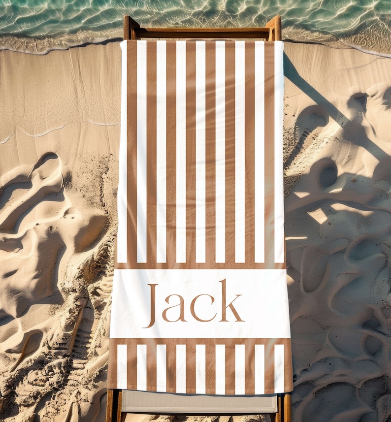 Puede incluir: Una toalla de playa a rayas marrones y blancas con el nombre "Jack" impreso en marr&oacute;n sobre una raya blanca.