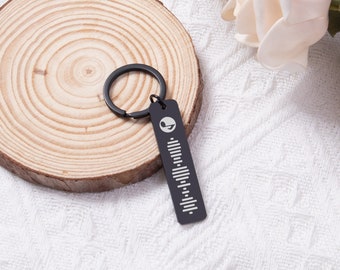 Könnte beinhalten: Schwarzer Schlüsselanhänger aus Metall mit einer silbernen Musiknote und einem Barcode-Design. Der Schlüsselanhänger ist an einem silbernen Ring befestigt.