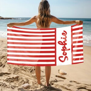 Puede incluir: Una toalla de playa a rayas rojas y blancas con el nombre "Sophie" escrito en cursiva blanca en la toalla.