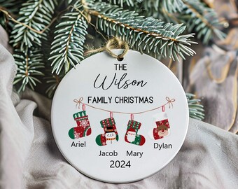 May include: White ceramic Christmas ornament with the text "The Wilson Family Christmas 2024" and four stockings with names "Ariel", "Jacob", "Mary", and "Dylan".