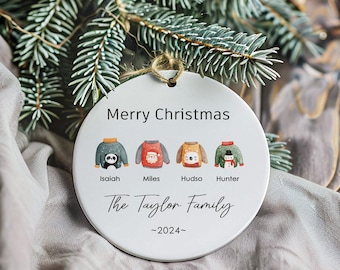 Può includere: Addobbo natalizio rotondo bianco con il testo "Buon Natale" e "The Taylor Family ~2024~" in nero. Sono raffigurati quattro animali dei cartoni animati con maglioni e nomi sotto: Isaiah, Miles, Hudso, Hunter.