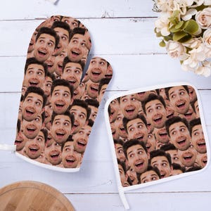 May include: A set of two oven mitts with a pattern of a man's face repeated across the surface. The mitts are white with a white trim. The mitts are on a white wooden surface.