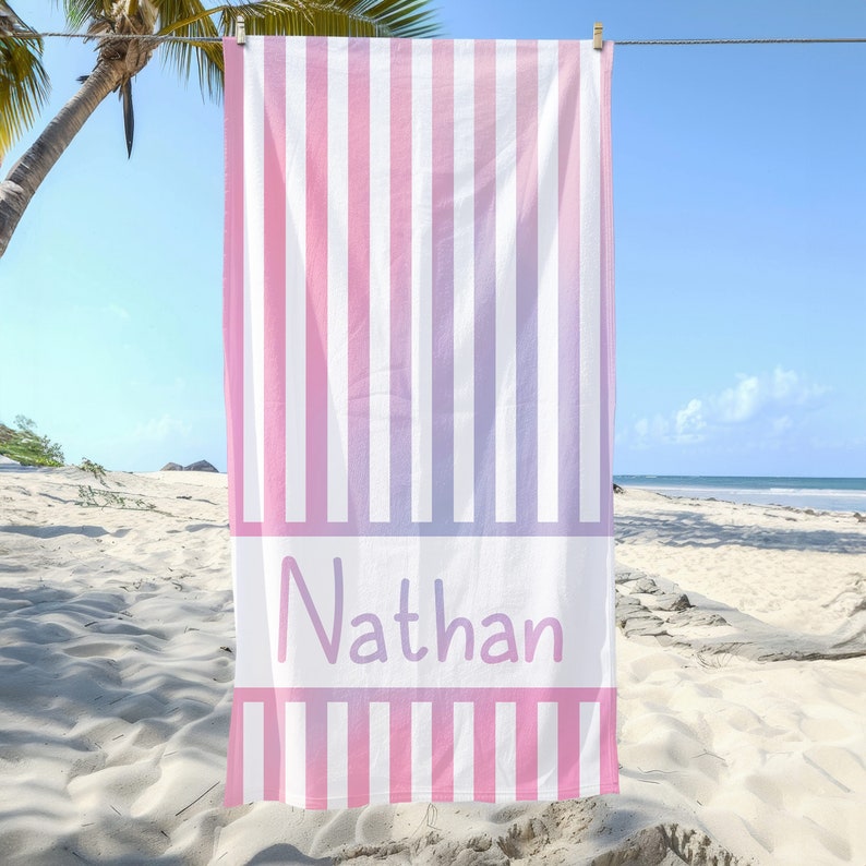 Puede incluir: Una toalla de playa a rayas rosa y blanca con el nombre "Nathan" impreso en morado en la parte delantera.