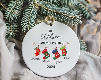 May include: White round Christmas ornament with the text "The Wilson Family Christmas 2024" and four stockings with names "Lincoln", "Micah", "Ryder", and "Cole" hanging from a string.