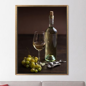 May include: A framed still life photograph of a bottle of white wine, a glass of white wine, a bunch of green grapes, and a corkscrew on a wooden table.