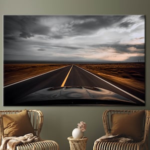 May include: A black car drives down a long, straight road with a yellow dividing line. The road is surrounded by brown, dry grass and a cloudy sky.