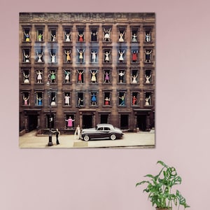 May include: A black and white photograph of a building with people in the windows. The people are all wearing different coloured clothing and are looking out of the windows. There is a black car parked in front of the building.