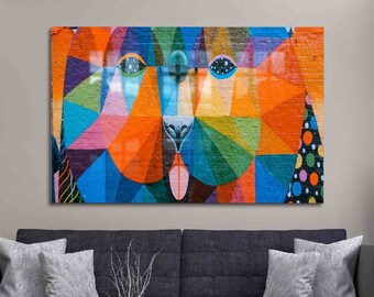 May include: A colorful geometric abstract painting of a dog's face. The painting is done in shades of blue, green, orange, pink, and yellow. The dog's eyes are large and black, and its tongue is sticking out.