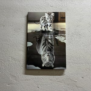 May include: A black and white image of a small kitten standing in a puddle of water. The kitten's reflection in the water appears as a large, white tiger.
