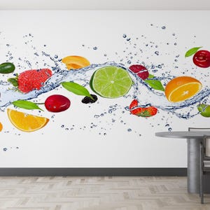 以下が含まれることがあります： さまざまな果物が入った、ダイナミックな水しぶきを描いた鮮やかな壁画。イチゴ、サクランボ、オレンジ、ライム、キウイが含まれており、カラフルで爽やかなディスプレイになっています。白い背景に、手前にダイニングテーブルがあります。